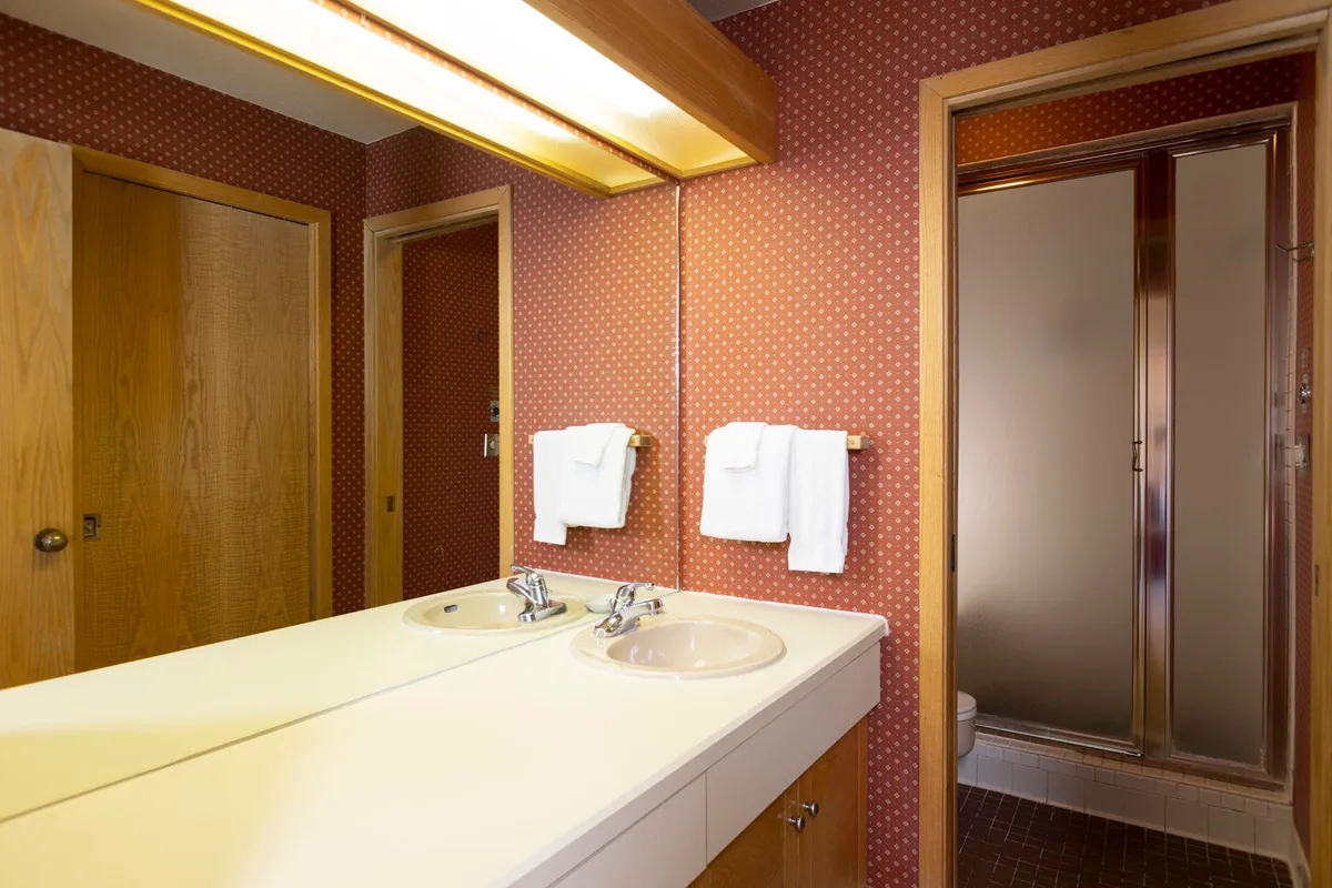 A modern bathroom with double sinks, a wide mirrored wall reflecting soft light, and a sleek shower enclosure. The space is neat, featuring ample room for morning and evening routines.